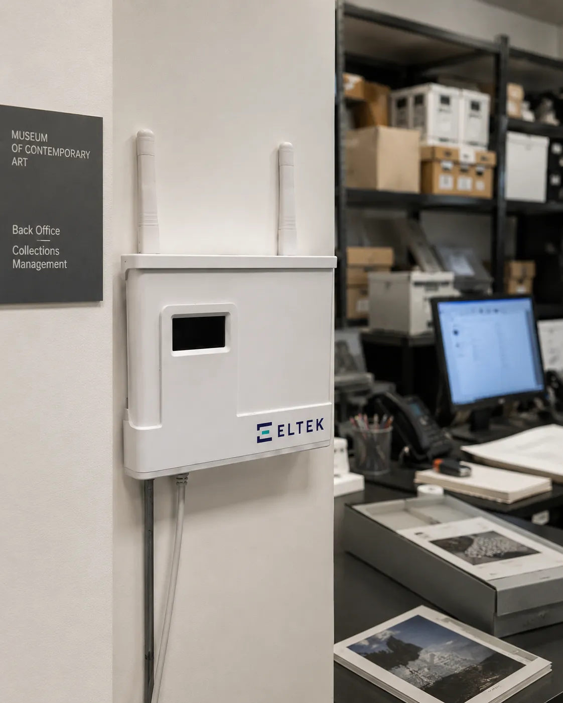 The Eltek Bridge (BRI-250), a white twin-antenna receiver unit, wall-mounted in a museum collections back-office and linking legacy Eltek transmitters into the Darca Solutions Suite