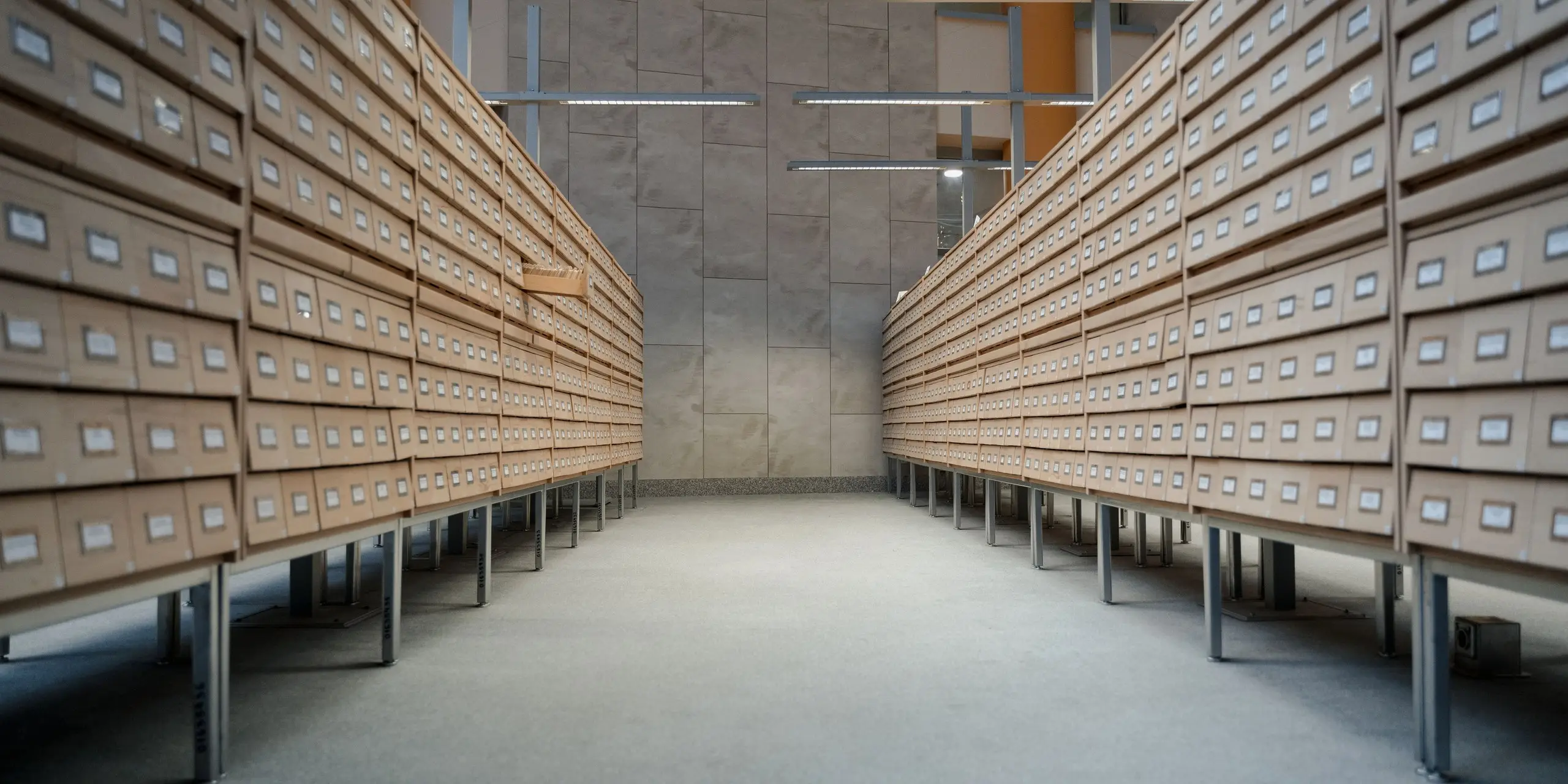 Rows of archival document boxes shelved down both sides of an aisle in a purpose-built store, the kind of packed archive stack where Eltek monitors temperature and humidity across every run of shelving