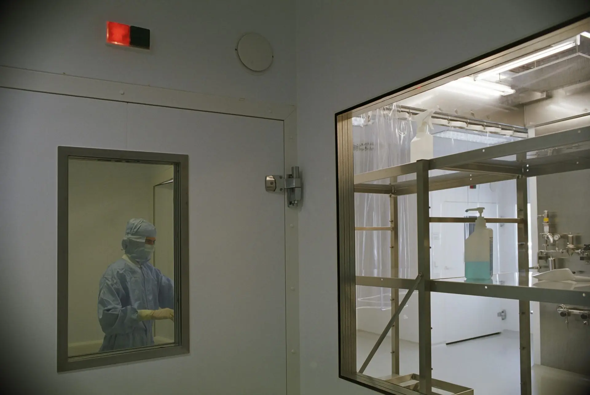 A gowned technician working inside a controlled cold-storage room, seen through its viewing window and warning light, the kind of critical space that keeps running unattended over the Christmas shutdown