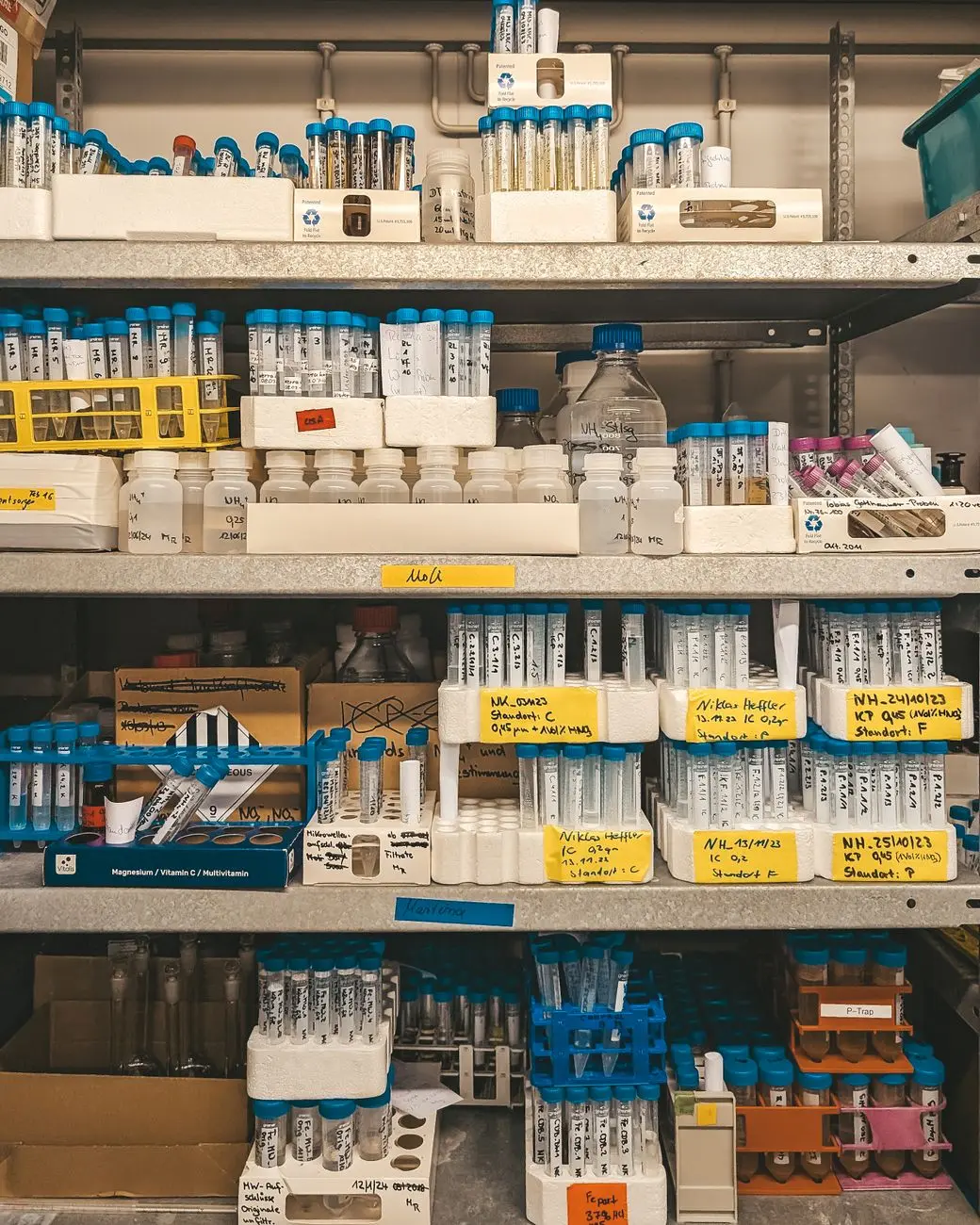 Laboratory shelves densely packed with labelled sample tubes and reagent bottles, the kind of multi-store sample estate a clinical laboratory has to keep within range and evidence