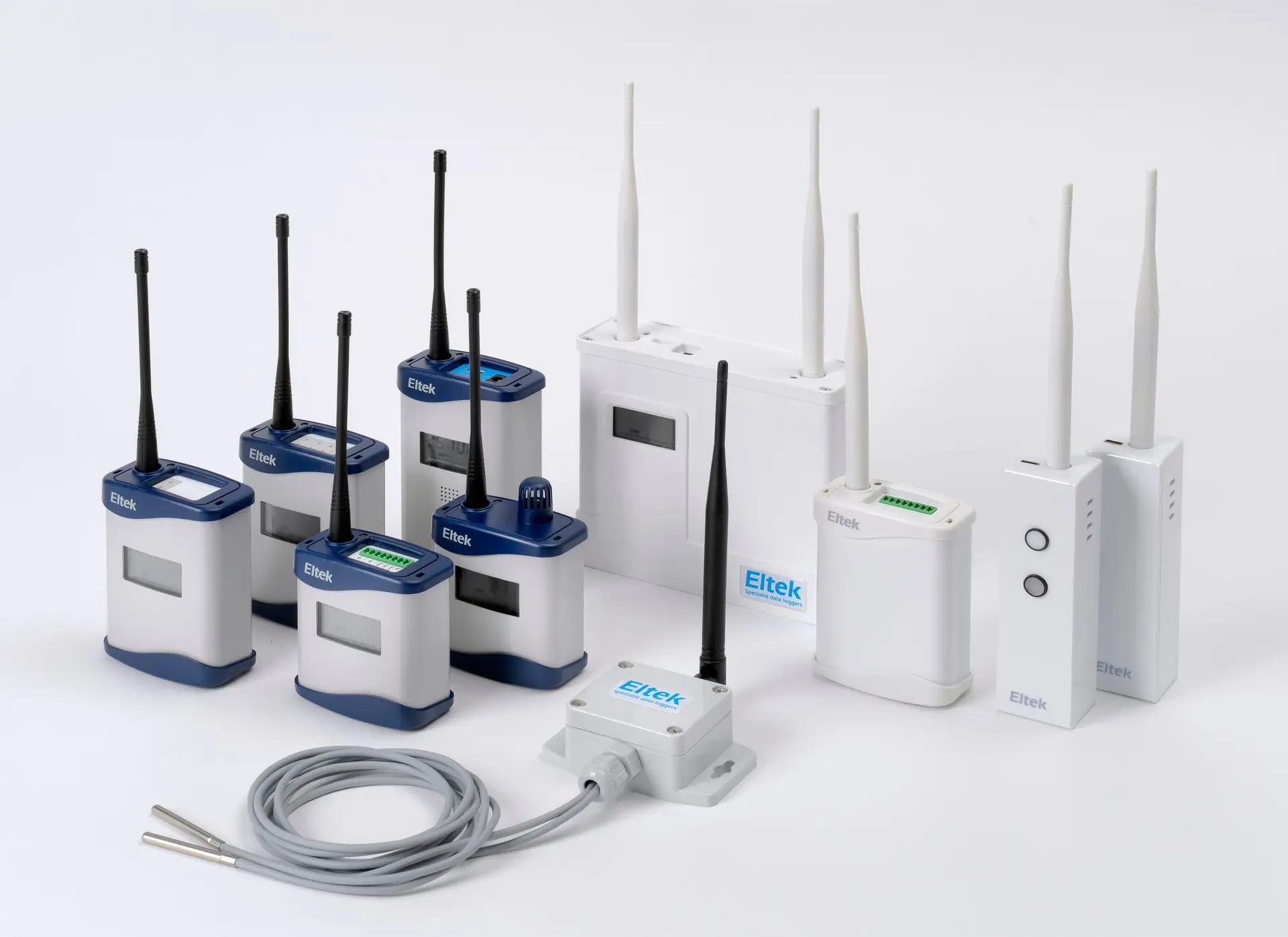 A group of Eltek wireless transmitters and sensors, navy-and-white units with aerials and a probe cable, arranged on a plain light background.