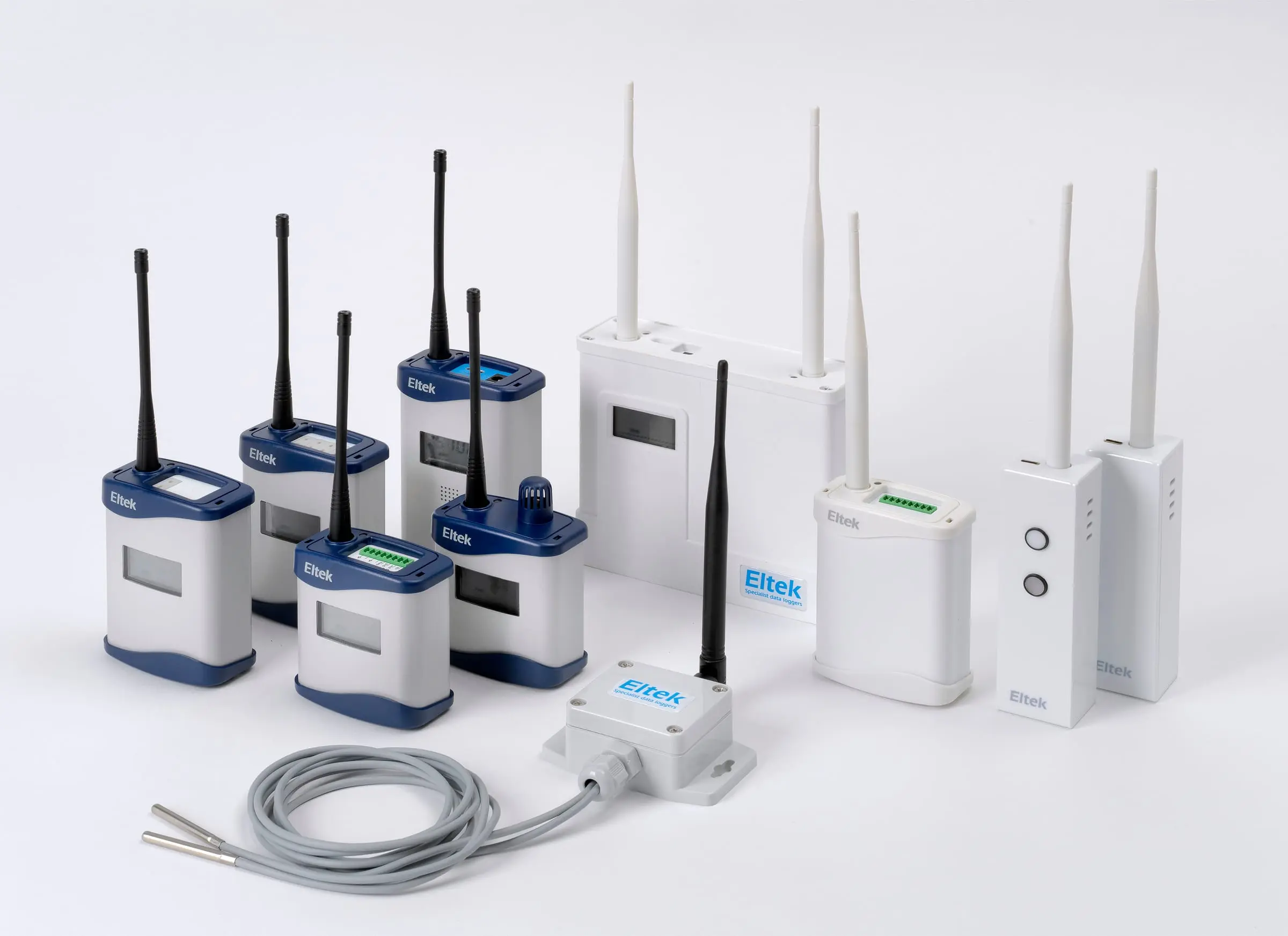 A group of Eltek wireless transmitters and sensors, navy-and-white units with aerials and a probe cable, arranged on a plain light background.