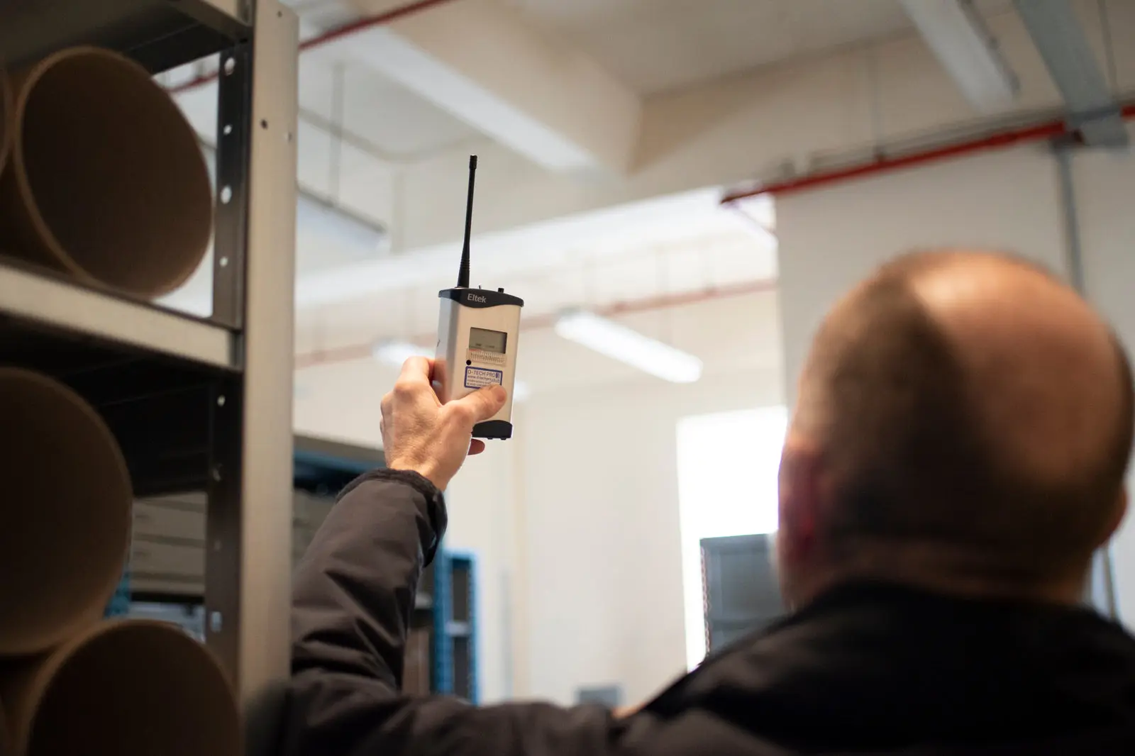 An Eltek engineer checking a wireless environmental sensor in a building interior, verifying indoor air quality and comfort monitoring coverage across the estate