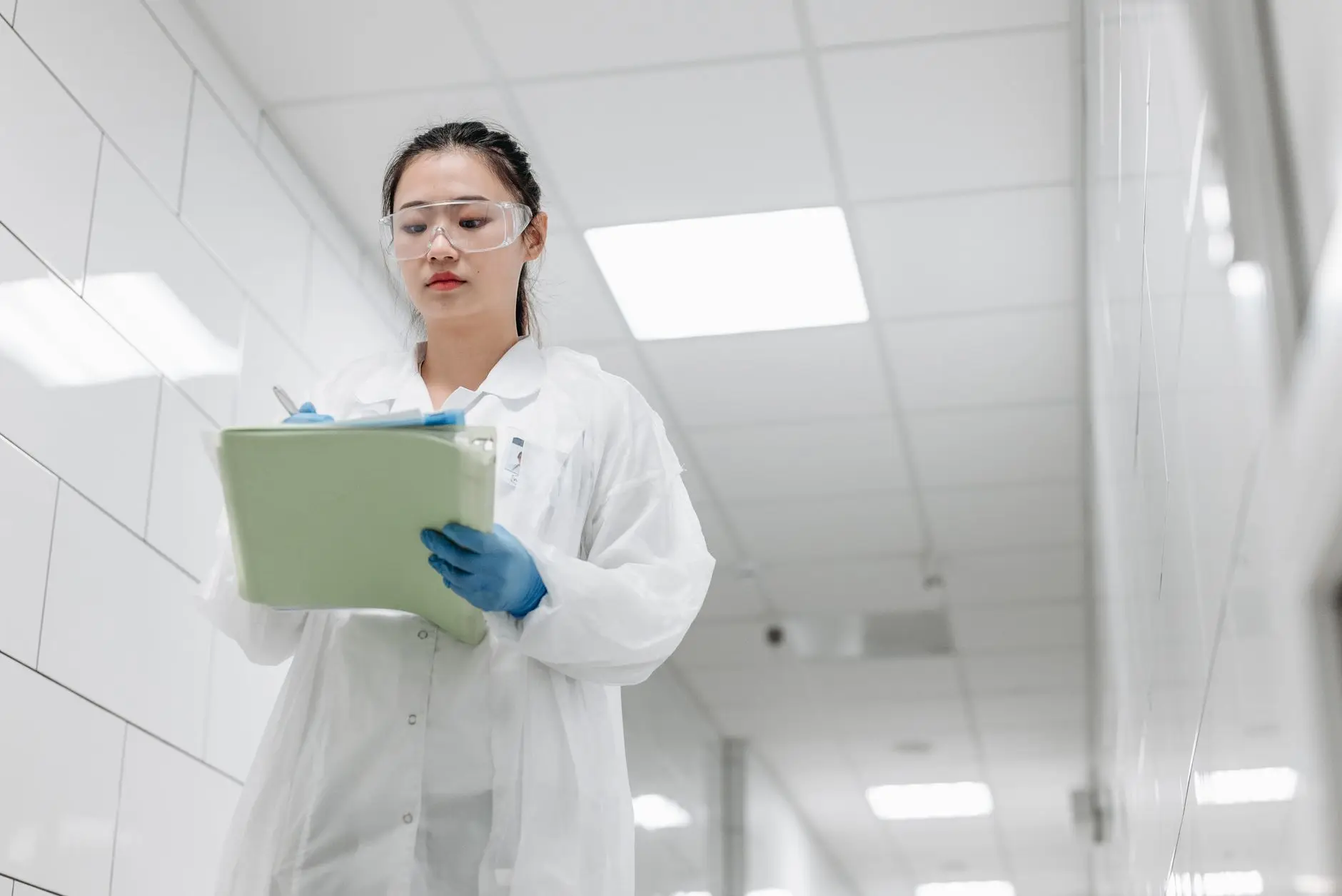 A laboratory technician recording a temperature reading by hand on a clipboard beside lab equipment