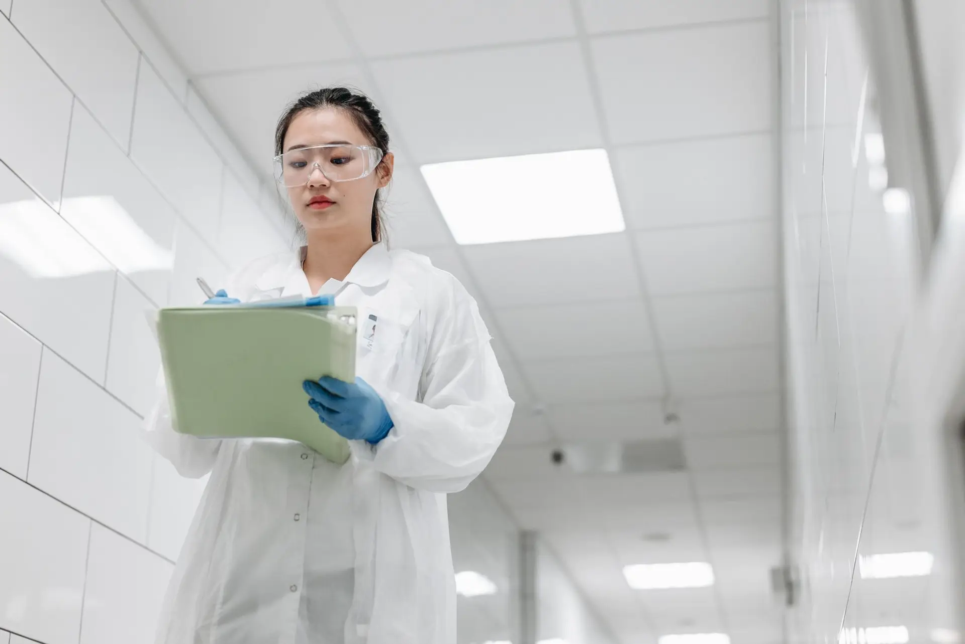 A laboratory technician recording a temperature reading by hand on a clipboard beside lab equipment