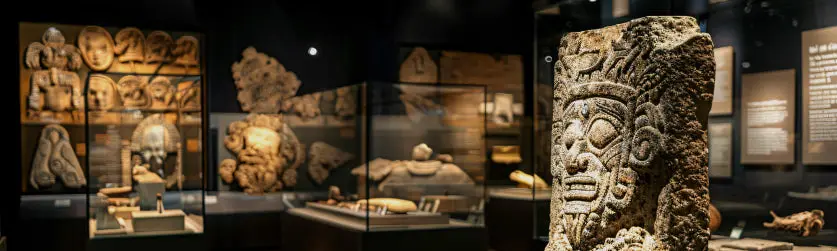 A dimly lit museum gallery of carved stone artefacts and sculpture displayed in glazed cases, the kind of heritage collection Eltek environmental monitoring is trusted to protect