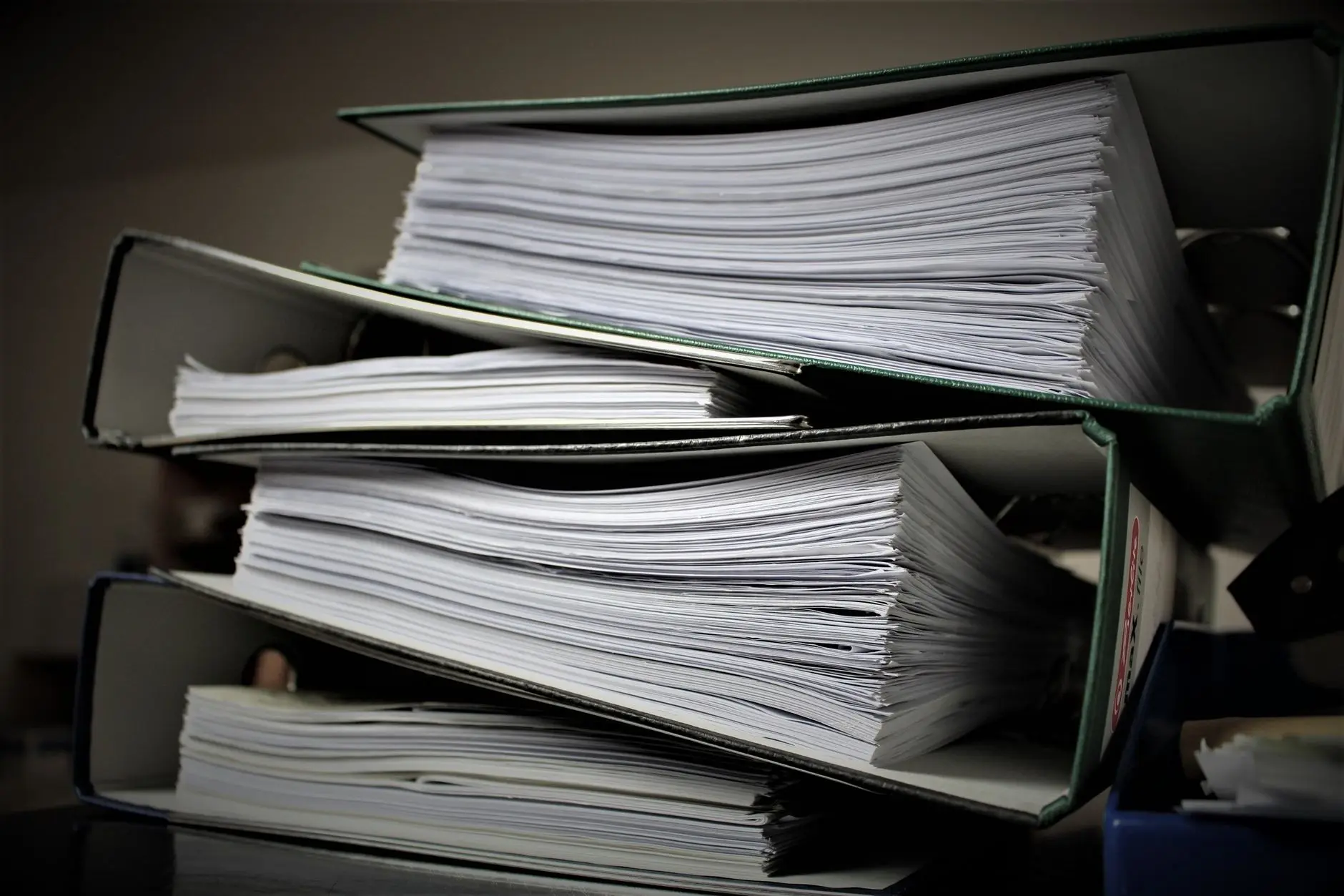 Overstuffed lever-arch binders full of printed temperature logs and manual records stacked on a desk