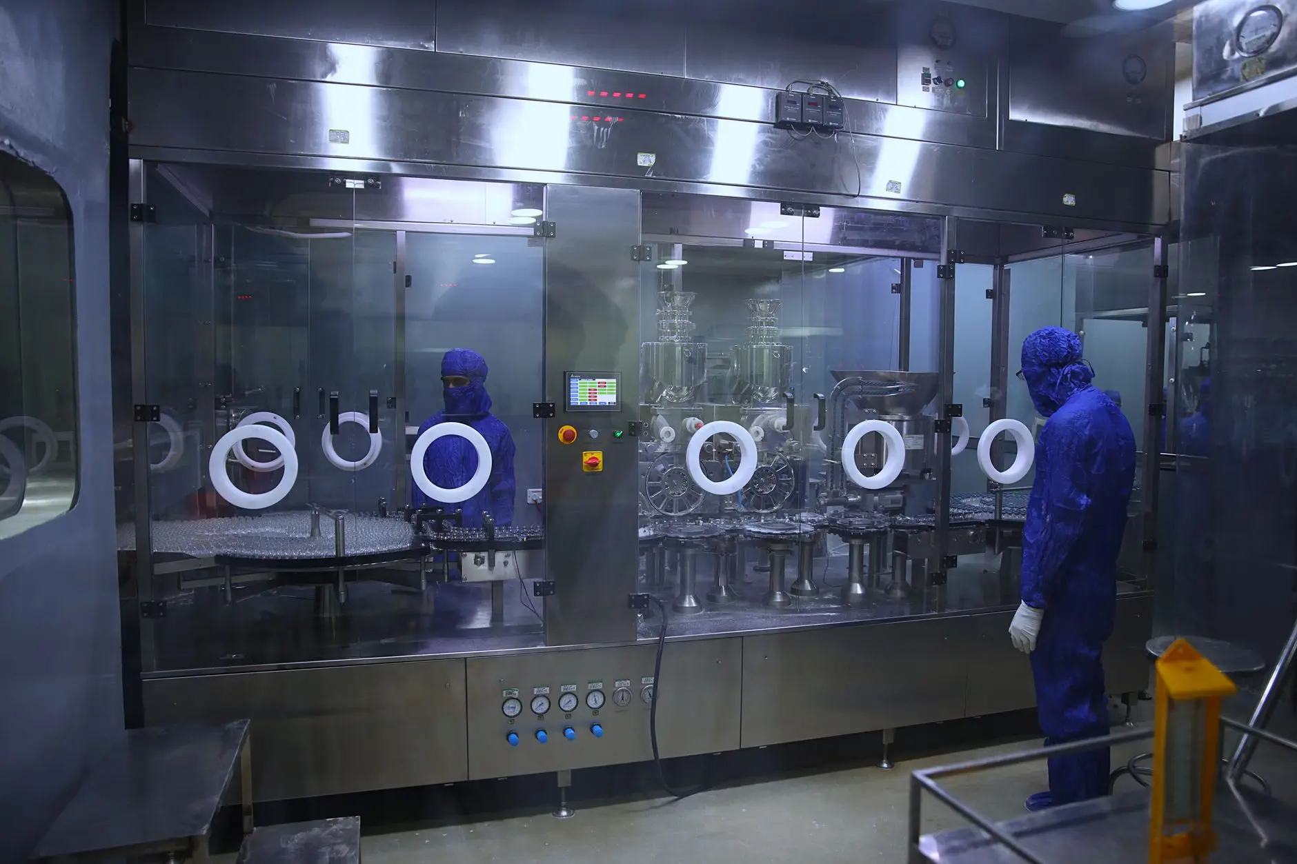 A sterile pharmaceutical manufacturing suite: an isolator filling line behind glass with an environmental control panel and gowned operators, the kind of regulated GMP environment Eltek monitors continuously with audit-ready records