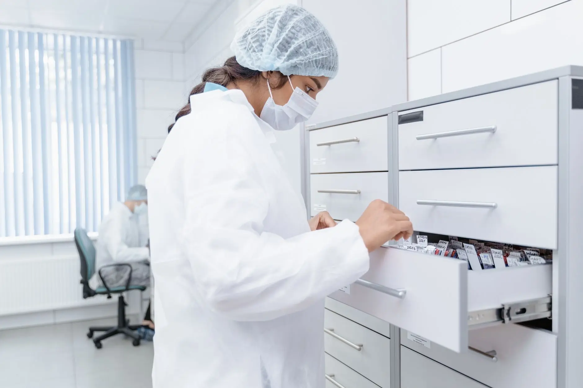 A researcher checking labelled samples in a laboratory storage drawer, the kind of sample-storage estate Eltek monitors continuously for research-governance traceability